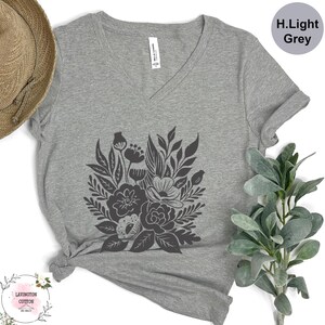 a gray t-shirt with a black floral design, a straw hat, and some greenery, all arranged on a white background.