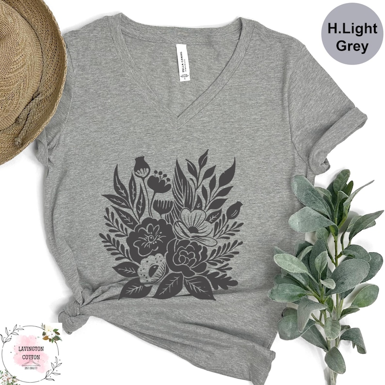 a gray t-shirt with a black floral design, a straw hat, and some greenery, all arranged on a white background.