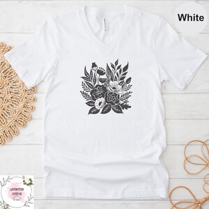 A white t-shirt with a black floral graphic printed on it, placed on a white wooden surface.