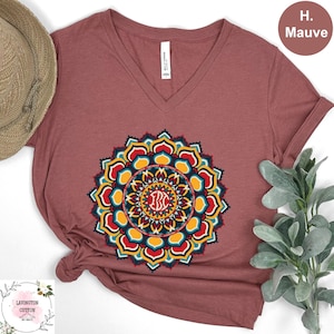 May include: Mauve V-neck t-shirt with a colorful mandala design. The mandala features red, yellow, blue, and teal accents, with the initials "BC" in the center. The shirt is made of cotton and has a relaxed fit.