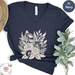 a navy blue t-shirt with a white floral design, placed on a white surface next to a straw hat and a green plant.
