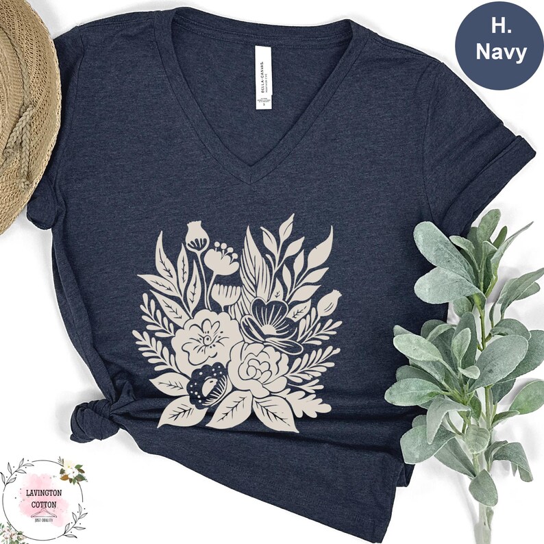 a navy blue t-shirt with a white floral design, placed on a white surface next to a straw hat and a green plant.