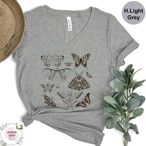 a grey t-shirt with a graphic design of various butterflies printed on it, along with a straw hat and some greenery.