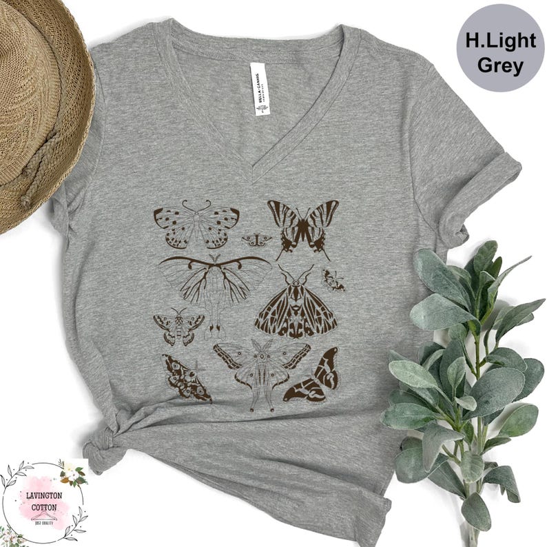 a grey t-shirt with a graphic design of various butterflies printed on it, along with a straw hat and some greenery.