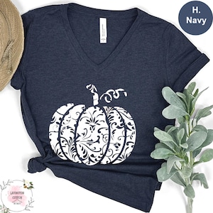 May include: Navy blue V-neck t-shirt featuring a white pumpkin design. The pumpkin is decorated with a floral pattern. The shirt is made of soft material. The shirt has the text "Lavington Cotton" on the bottom left.