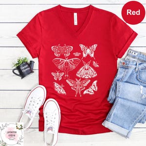 a red V-neck t-shirt with a white butterfly design, a pair of white sneakers, a pair of blue jeans, and a small black teapot.
