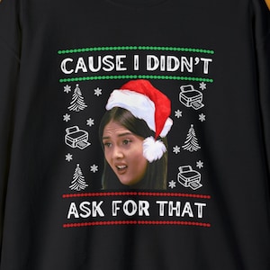 May include: Black Christmas sweater with a red and white design. The sweater features a woman's face with a Santa hat and the text "Cause I didn't ask for that".