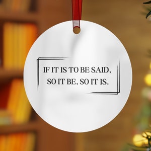 May include: White round Christmas ornament with a black border and the text "IF IT IS TO BE SAID, SO IT BE, SO IT IS." hanging from a red ribbon on a Christmas tree.