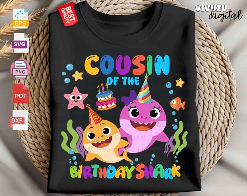 Puede incluir: Una camiseta negra con un gr&aacute;fico colorido y el texto "COUSIN OF THE BIRTHDAY SHARK". El dise&ntilde;o incluye dos tiburones de dibujos animados con gorros de fiesta, un pastel de cumplea&ntilde;os con velas encendidas, una estrella de mar rosa y burbujas.