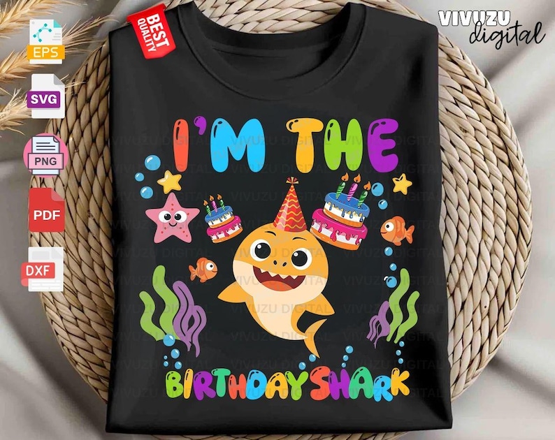 Puede incluir: Una camiseta negra con un gr&aacute;fico colorido de un tibur&oacute;n de dibujos animados con un gorro de fiesta, rodeado de dos pasteles de cumplea&ntilde;os, una estrella de mar, dos peces naranjas peque&ntilde;os y algas verdes y moradas. El texto dice I'M THE BIRTHDAY SHARK.
