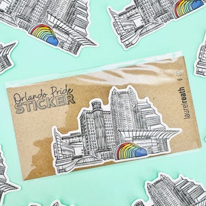 Puede incluir: Una hoja de pegatinas con seis pegatinas que muestran una ilustraci&oacute;n en blanco y negro del horizonte de Orlando con un arco&iacute;ris sobre los edificios. La hoja de pegatinas tiene el texto "Orlando Pride STICKER".