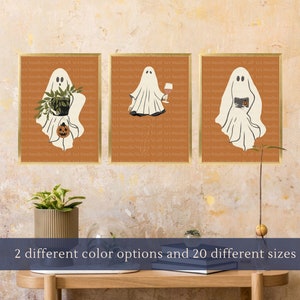 Pode incluir: Três impressões emolduradas com um fantasma branco em cada uma. O fantasma da impressão da esquerda está segurando uma planta em vaso, o fantasma da impressão do meio está segurando uma taça de vinho e o fantasma da impressão da direita está segurando um livro. As impressões estão em uma parede com um fundo laranja.