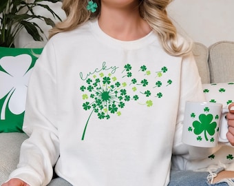 Puede incluir: Sudadera blanca con un diseño de diente de león de trébol verde y la palabra "lucky" escrita en cursiva.