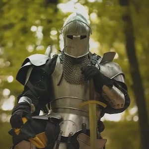 Op de afbeelding: Een ridder in volledige bepantsering knielt in een bosrijke omgeving. De zilverkleurige bepantsering omvat een helm, maliënkolder, schouderbeschermers en beenbescherming. Een geel en goudkleurig zwaard wordt rechtop gehouden. De ridder draagt zwarte handschoenen.