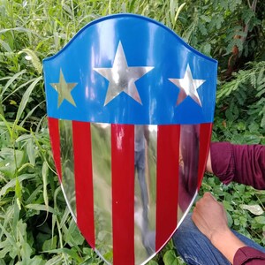 May include: A red, white, and blue shield with a silver star design. The shield is made of metal and has a slightly curved shape.