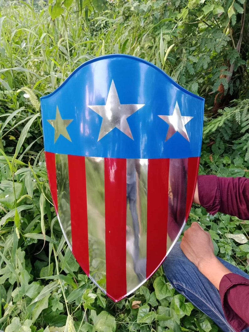 May include: A red, white, and blue shield with a silver star design. The shield is made of metal and has a slightly curved shape.