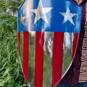 May include: A red, white, and blue shield with a silver star design. The shield is made of metal and has a slightly curved shape.