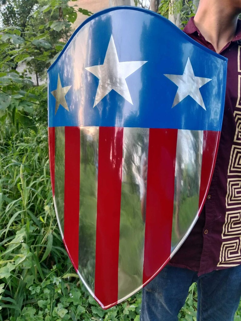 May include: A red, white, and blue shield with a silver star design. The shield is made of metal and has a slightly curved shape.