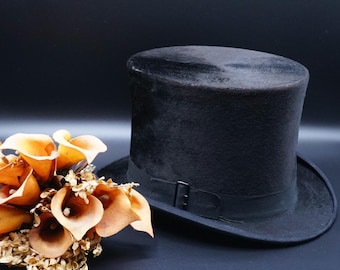 May include: A black top hat with a black band and a buckle. The hat is made of felt and has a smooth finish.