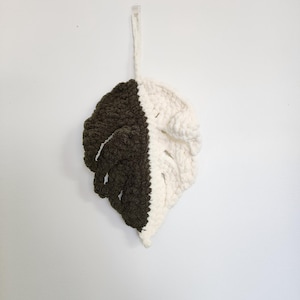 Puede incluir: Un colgante de pared de hoja de ganchillo en color marrón y blanco. La hoja está hecha de hilo y tiene una superficie texturizada.