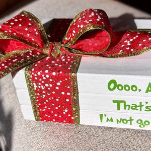 May include: A white wooden gift box with a red ribbon featuring white polka dots and gold trim. The box has green text that reads "Oooo, Ahhh, That's it, I'm not going."