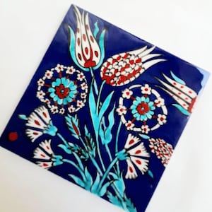 May include: Square ceramic tile with a vibrant floral design. The tile features a deep blue background with a bouquet of flowers in white, red, and turquoise. The flowers include tulips and other stylized blooms.