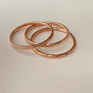 Puede incluir: Tres anillos apilables de oro rosa. Los anillos son simples y delicados, con una textura martillada.