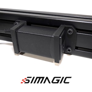 May include: Close-up of a black component attached to a black metal frame. The component has a ribbed texture and is secured with screws. The SIMAGIC logo is visible at the bottom.