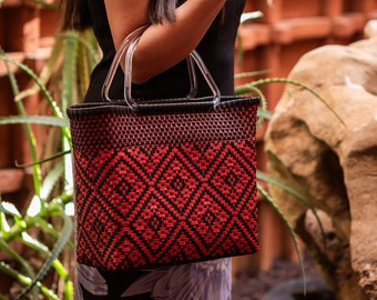 Handmade hand-woven bag made of recycled plastic with a black base and red design, with transparent plastic handles.
