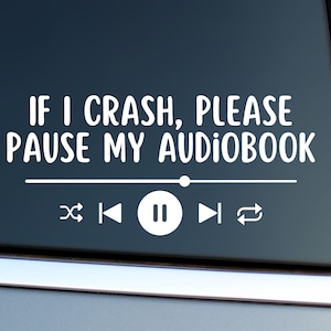 May include: White vinyl decal with the text "IF I CRASH, PLEASE PAUSE MY AUDIOBOOK" above a media player control bar. The controls include skip backward, play/pause, skip forward, and repeat icons.