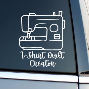 May include: White outline of a sewing machine with the text "T-Shirt Quilt Creator" in a script font. The image is a decal, likely for a car window or similar surface. The design is simple and clean, suitable for crafters.