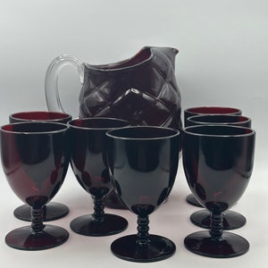 Puede incluir: Un juego de ocho vasos para beber de vidrio rojo oscuro, que incluye una jarra y siete copas de vino. La jarra tiene un diseño acolchado y las copas tienen una base con tallo.