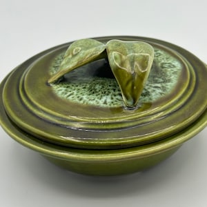 May include: A green ceramic bowl with a lid. The lid has two leaf-shaped handles.