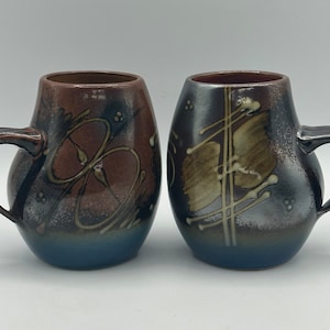Peut inclure: Deux tasses en céramique avec des motifs abstraits bruns, bleus et blancs. Les tasses ont une forme arrondie et une anse.