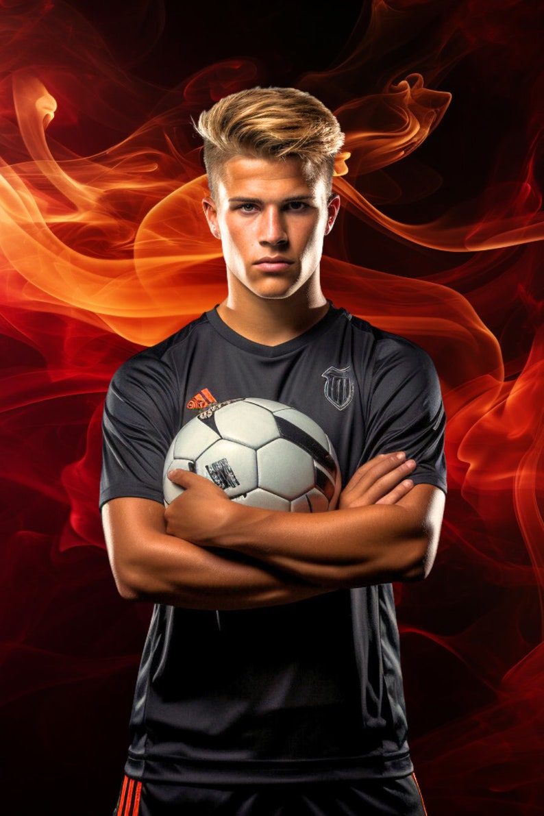 May include: A young man in a black soccer jersey with a white soccer ball in his arms. He is standing in front of a red and orange smoke background.
