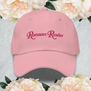 Może przedstawiać: Różowa czapka z daszkiem z haftem "Romance Reader" w kolorze różowym z przodu.