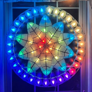 May include: A large, circular, star-shaped, paper lantern with a white center and a multi-colored border. The lantern is decorated with small, white lights that create a glowing effect.