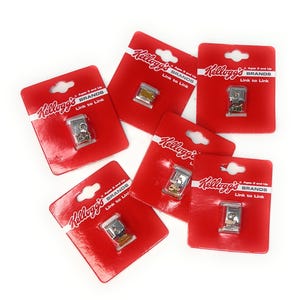 May include: A collection of Kellogg's Brands Link to Link promotional items. Each item is packaged on a red card with the Kellogg's logo and text. The small, metallic charms are visible through the clear plastic packaging.