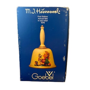 Puede incluir: Caja azul con el texto "M.J. Hummel" y "First Edition Annual Bell in bas-relief 1978". La caja contiene una campana con un mango color crema y una campana amarilla con un niño tocando el acordeón.