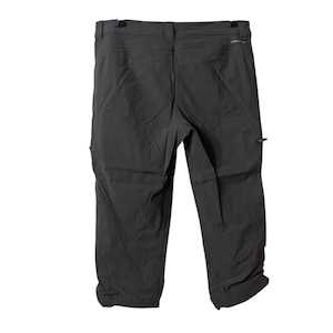 Pode incluir: Calças de exterior cinza escuro com fecho de botão, presilhas para cinto e bolsos com zíper. As calças são feitas de um material leve e durável, adequado para caminhadas ou outras atividades ao ar livre.