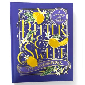 May include: A purple book with gold lettering that reads "Bitter & Sweet" and a gold ribbon with the text "Tsh Oxenreider". The book cover features a lemon and flower design and a gold circle with the text "A Journey into Easter".