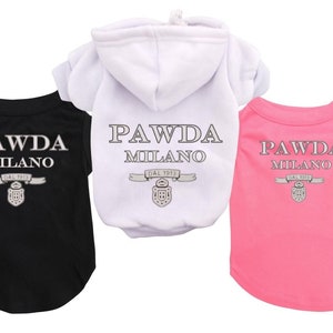 May include: Three dog shirts, one black, one white, and one pink, all with the same logo: "PAWDA MILANO DAL 1913" with a crest. The white shirt is a hoodie.