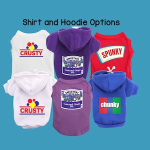 May include: Five different dog shirts and hoodies. Two white hoodies with the word "CRUSTY" in red and yellow. A purple hoodie with a grape jelly label that says "SWEETEST Concord Grape Jelly". A red shirt with the word "SPUNKY" in white and blue. A blue hoodie with the word "chunky" in red, white, and green.