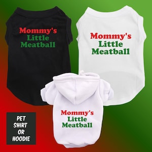 May include: Three pet shirts or hoodies in black, white, and white. Each garment has the text "Mommy's Little Meatball" in red and green. The background is a gradient of red and green.