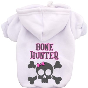 Op de afbeelding: Witte hoodie voor honden met een roze schedel en gekruiste botten afbeelding en de tekst "BONE HUNTER" in roze.