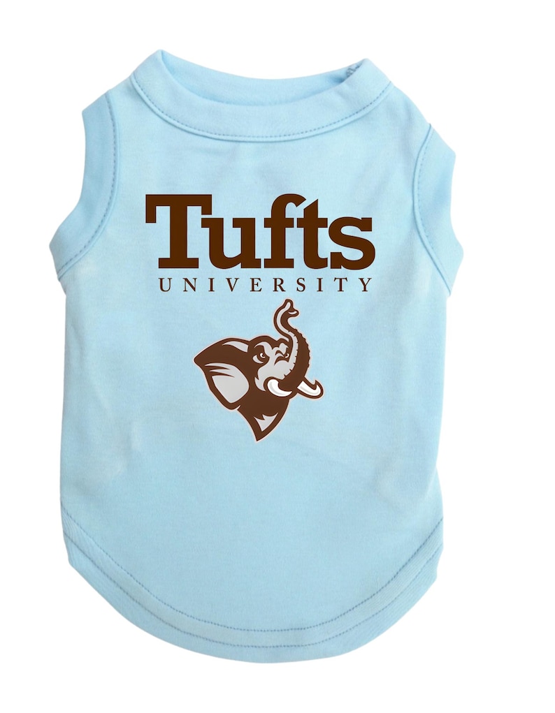 May include: Light blue dog shirt with the text "Tufts UNIVERSITY" in brown block letters. A brown elephant logo is below the text. The shirt is sleeveless and made of a soft material.