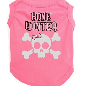 Op de afbeelding: Roze sleeveless hondenshirt met een witte schedel en gekruiste beenderen afbeelding en de tekst "BONE HUNTER" in zwart.