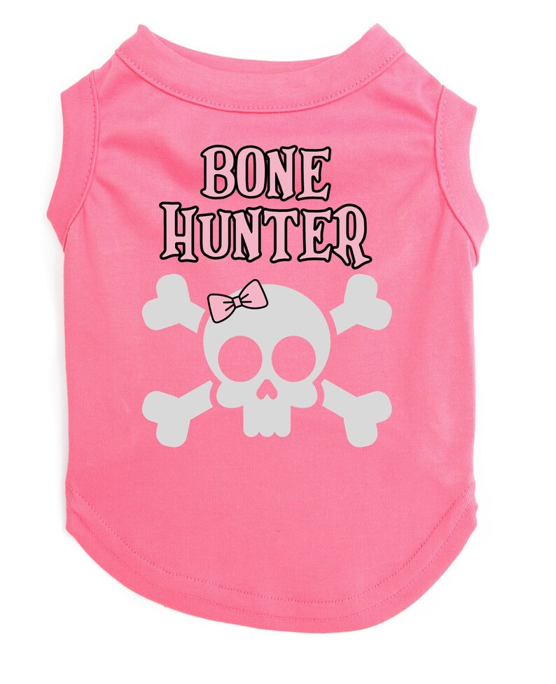Op de afbeelding: Roze sleeveless hondenshirt met een witte schedel en gekruiste beenderen afbeelding en de tekst "BONE HUNTER" in zwart.