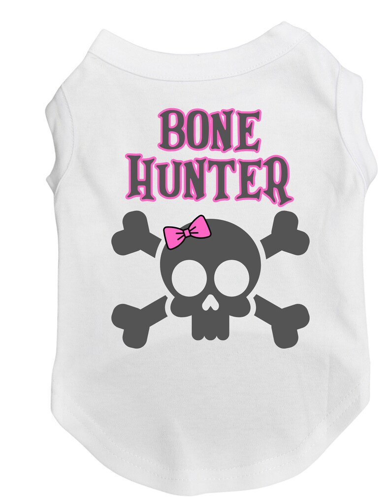 Op de afbeelding: Witte hondenshirt met een roze schedel en gekruiste beenderen ontwerp. De tekst "BONE HUNTER" is in roze letters op het shirt gedrukt.
