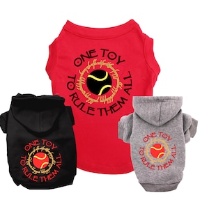 Puede incluir: Tres camisetas para perros en rojo, negro y gris. Cada camiseta presenta un gráfico de una pelota de tenis con el texto "One Toy To Rule Them All".